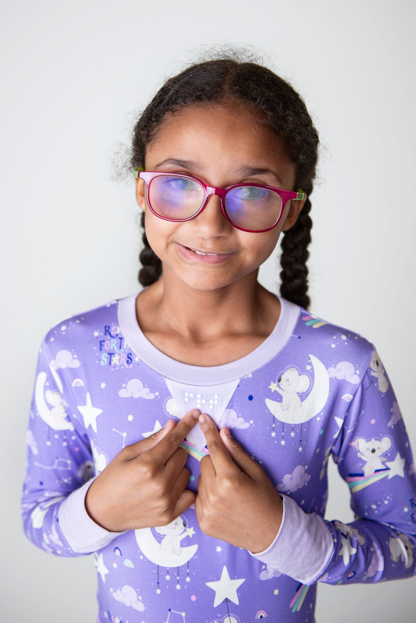 Close up of braille on Pajamas with Visually Impaired Girl wearing the space-themed design, pink glasses and pointing to the braille