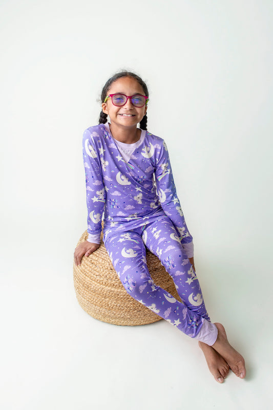 Visually Impaired girl sitting on a cushion wearing Purple bamboo kids pajamas featuring a Koala in space theme