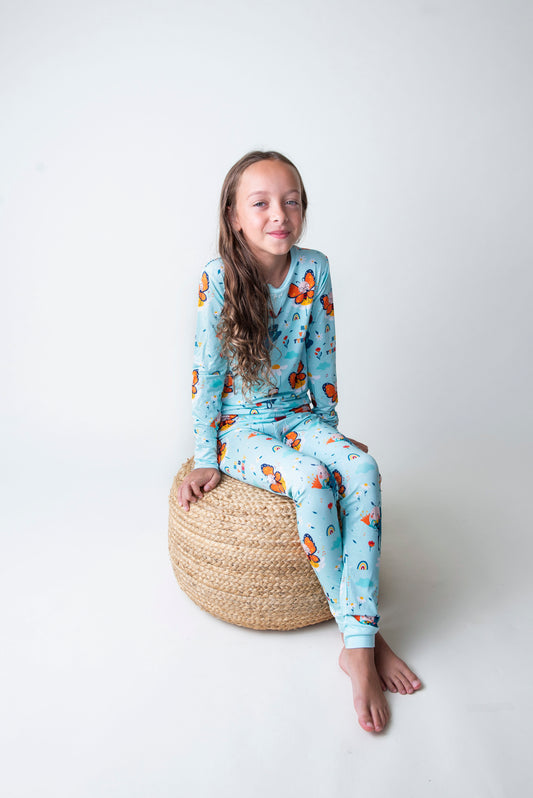 Young girl wearing a butterfly patterned pajama set sitting on a woven stool against a white background